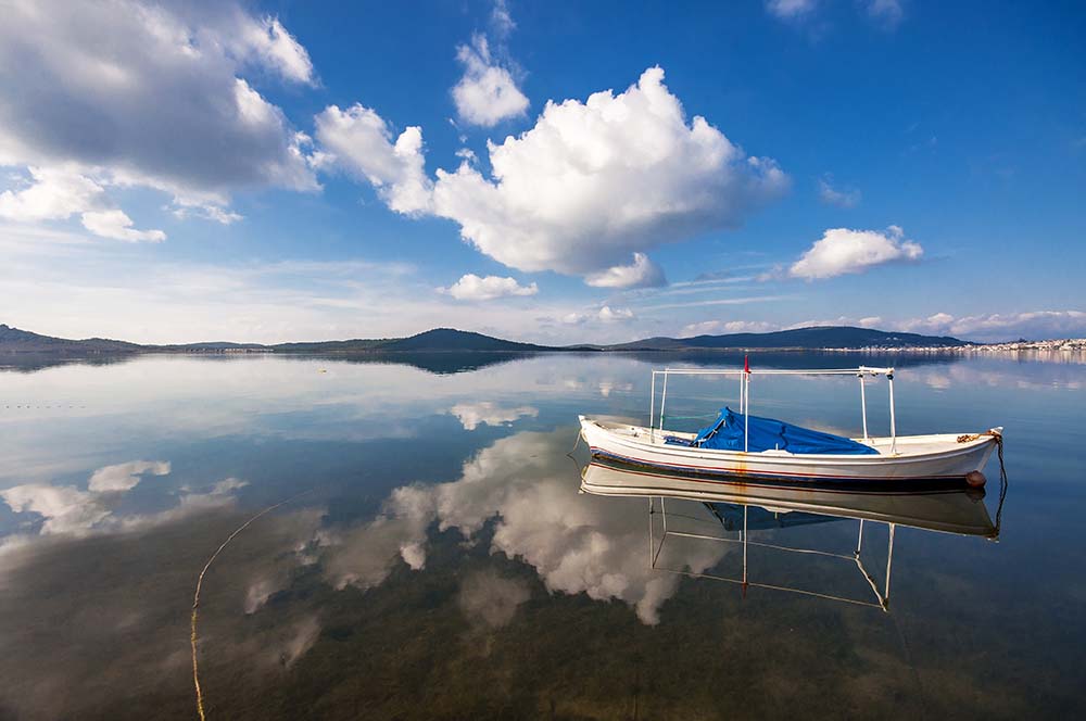 Fishing boat and clouds reflections at calm day in Ayvalik